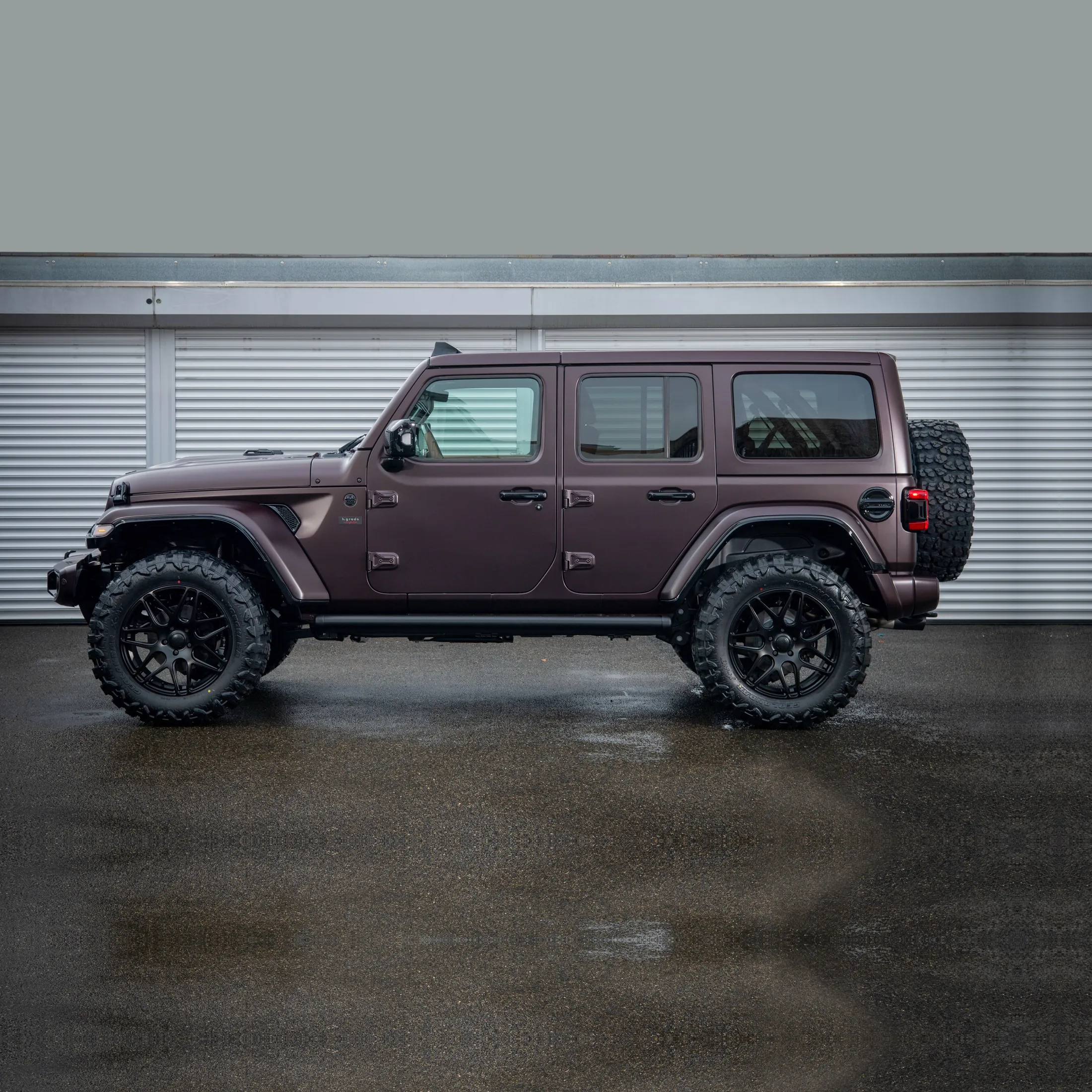 Seitenansicht eines von h.grade veredelten Jeep Wrangler in mattem Lila: Höherlegung, Geländereifen auf schwarzen Rädern, Seitenrohr und Reserverad am Heck.